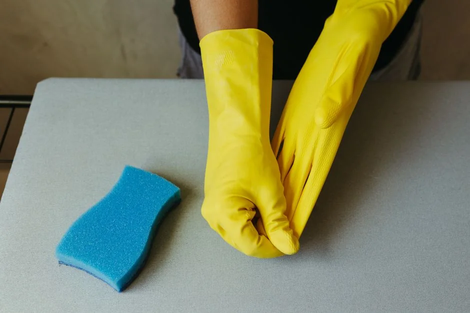 Une personne entièrement équipée en EPI désinfecte une table à l’intérieur, pour l’hygiène et la sécurité.